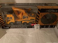 Photo of boxed new 1:15 scale excavator radio control toy by Playtek, visible through clear plastic window, showing the yellow excavator and remote control disc