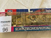 Photo showing front and side view of the die-cast tractor-trailer model in original packaging, showcasing the gold St. Louis Rams graphics and NFL logo.