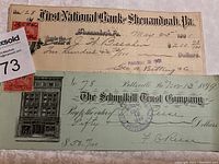 Two vintage bank checks laid out flat, one from 1901 and one from 1899 with detailed handwriting, stamps, and printed bank names.
