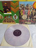 Photo of album cover showing colorful collage and yellow circular Limited Original Marble Vinyl Edition sticker, alongside the translucent marble vinyl record laying on an inner sleeve.