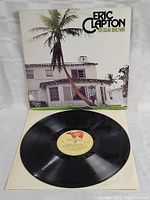 Vinyl LP record with beige label on white inner sleeve, front cover of album with white house and palm trees, 'Eric Clapton 461 Ocean Boulevard' text.