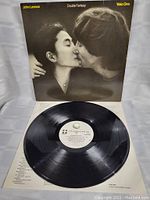 Close-up of vinyl record showing clean black vinyl and white center label with track info; also shows LP partially pulled out of cover.