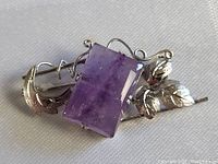 Close-up photo of the rectangular amethyst gemstone set in a sterling silver brooch with leaf and vine decorative elements.