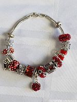 Full view of Pandora sterling silver charm bracelet with various red and silver Christmas-themed charms on white fabric background.