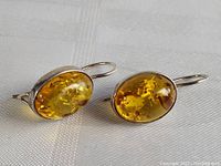 Pair of oval-shaped amber earrings set in sterling silver bezels with lever-back hooks, shown on white textured fabric.