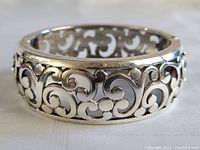 Close-up side view of the silver bracelet showing the cut-out scroll design and polished surface.