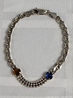Full bracelet laid flat showing silver chain and two colored stones with beaded detail