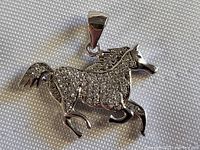 Front perspective of silver horse pendant with clear stones on body and polished silver bail.
