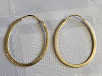 Pair of oval shaped gold tone brushed sterling silver earrings on a white textured background.