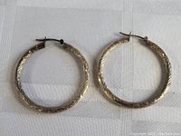 Top down view of the pair of sterling silver large carved hoop earrings placed on white fabric showing carved details and closure mechanism.