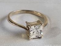 Close-up of sterling silver ring band and square clear stone showing prong setting and light wear.