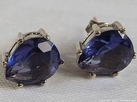 Close-up photo showing front view of both earrings highlighting the pear-shaped blue sapphires in sterling silver prong settings.