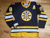 Front angle of black and yellow Boston Bruins jersey with large B logo and number 8 on sleeves, showing tags near hem.