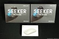 Two Delux Seeker M618XSD boxed mice and one Microsoft Surface Mobile Mouse boxed, displayed on black background