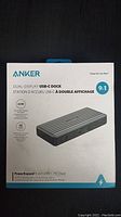 Front of box showing product name, image, and key features like 60W charging, dual display, 4K display support.