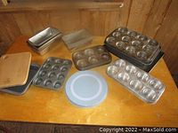 Overview of various metal baking pans including bread pans, cookie sheets, cupcake pans, and a wooden cutting board on a wooden table.