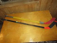 Two ball hockey sticks displayed on wooden surface, showing full length of sticks.