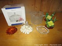 Photo showing crystal covered candy dish box, ice bucket, amber glass dish, clear glass oval dish, octopus figurine on coral, and two porcelain hummingbirds on a wooden surface.