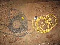 Photo of coiled black and yellow extension cords on wooden floor, showing ends and plugs