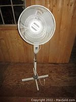 Full view of large white floor fan standing on wooden floor with cross base and power cord attached.