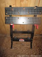 Full view of Job Mate folding work bench open and standing upright with two adjustable wooden panels on top showing measurement markings and clamp holes.