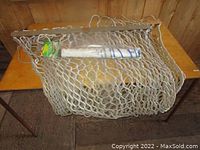 White rope hammock folded on table showing rope weave and wooden spreader bars.