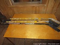 Four right handed hockey sticks lying on a wooden table, showing full length and blades touching table.