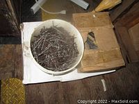 Bucket filled with generic nails and a damaged cardboard box beside it containing nails.