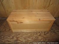 Front and side view of the rectangular pine wood box on wooden floor, showing hinged lid closed.