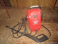 Front view of the red Powerwasher pressure washer sitting on wooden floor showing hose and spray gun.