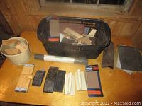 Lot of sanding blocks and sandpaper sheets placed on a wooden table, showing a variety of sanding tools including wooden and plastic blocks, and sandpaper pieces.