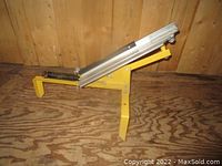 Side view of the skeet thrower showing yellow metal base, aluminum throwing arm, and black tension spring.