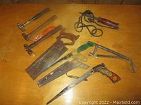 Overview of assorted hand tools on wooden surface including hand saws, hammers, coping saw, and rasp file.