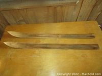 Two small wooden skis with pointed tips laid side by side on a wooden surface.