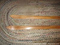 Pair of vintage wooden skis laid on braided oval rug showing tips and smooth wood texture.