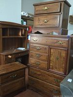 Photo showing one tall wooden dresser with multiple drawers, cabinet door, armrest curve bottom, and back panel detached. Also shows two wooden nightstands with two drawers each and brass handles. Furniture shows scratches and wear.