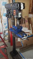 Front-side view of Guardian Power 12-speed heavy duty drill press with mounted blue Central Forge 6-inch cross slide vise in workshop area.