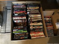 Top view of two open boxes filled with DVDs and the DVD storage rack next to them on the floor.
