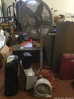 Overall photo showing all four devices including fans and heaters, with extension cord and surrounding area. Provides view of item size and general condition.