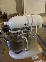 White KitchenAid Classic K45SSWH stand mixer with stainless steel bowl attached and power cord wrapped around mixer arm.