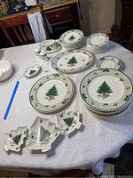 Overview of entire dinnerware set laid out on white tablecloth, showing plates, serving dishes, and holiday-themed dishes.