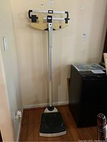 Full view of the beige Seca mechanical scale standing on wooden floor near a wall and cabinet.