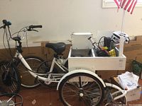 Full view of white adult battery-powered tricycle with wooden cargo box, wire basket and US flag mounted at rear