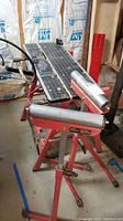 Photo of red metal workbench with black top that has measurement markings, showing overall structure and step platform.