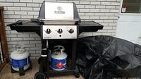 Front view of Broil King Monarch grill with side shelves, control panel, two propane tanks and cover