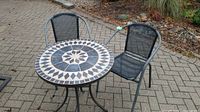 Overall view of bistro set including round mosaic tile tabletop on metal frame and two mesh chairs.