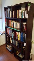 Front view of the dark wooden bookshelf filled with books to illustrate its compartments and size.