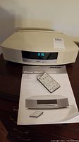 Front view of Bose Wave Music System with digital clock display showing 3:19, remote and manual on tabletop