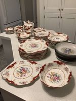 Full view of counters displaying stacks of red-and-gold-bordered china plates, bowls, cups, saucers, and serving pieces
