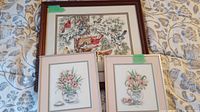 Full view of the three framed cross stitch pieces laid on fabric background. The largest features birds and the two smaller frames show floral compositions.